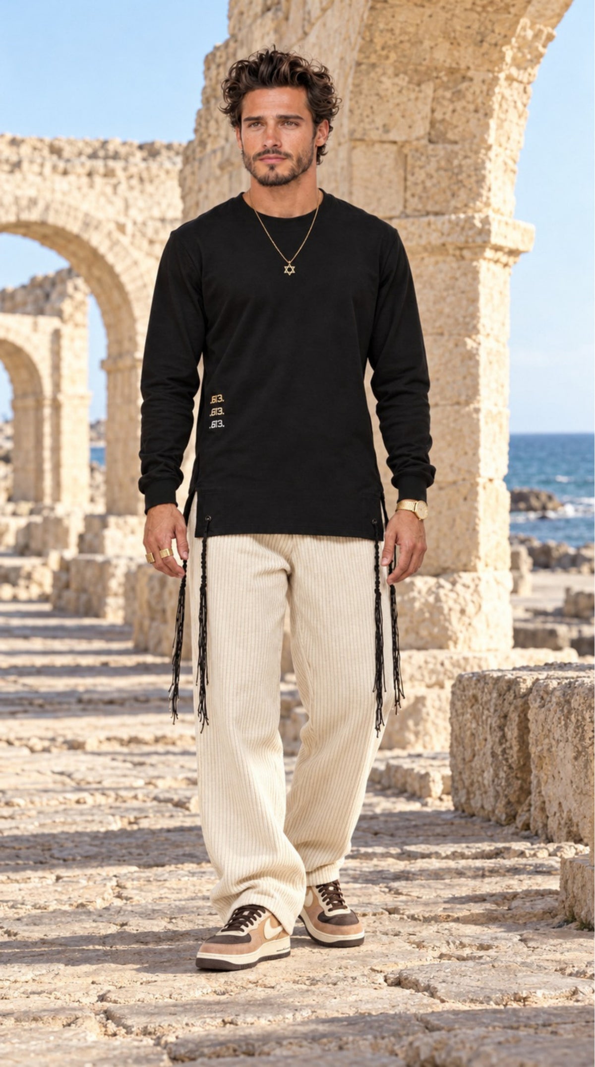 True Balance של 613, חולצת ציצית שחורה עם שרוול ארוך, צילום חוץ לצד מבני אבן