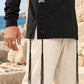 True Balance של 613, חולצת ציצית שחורה עם שרוול ארוך, צילום חוץ לצד מבני אבן