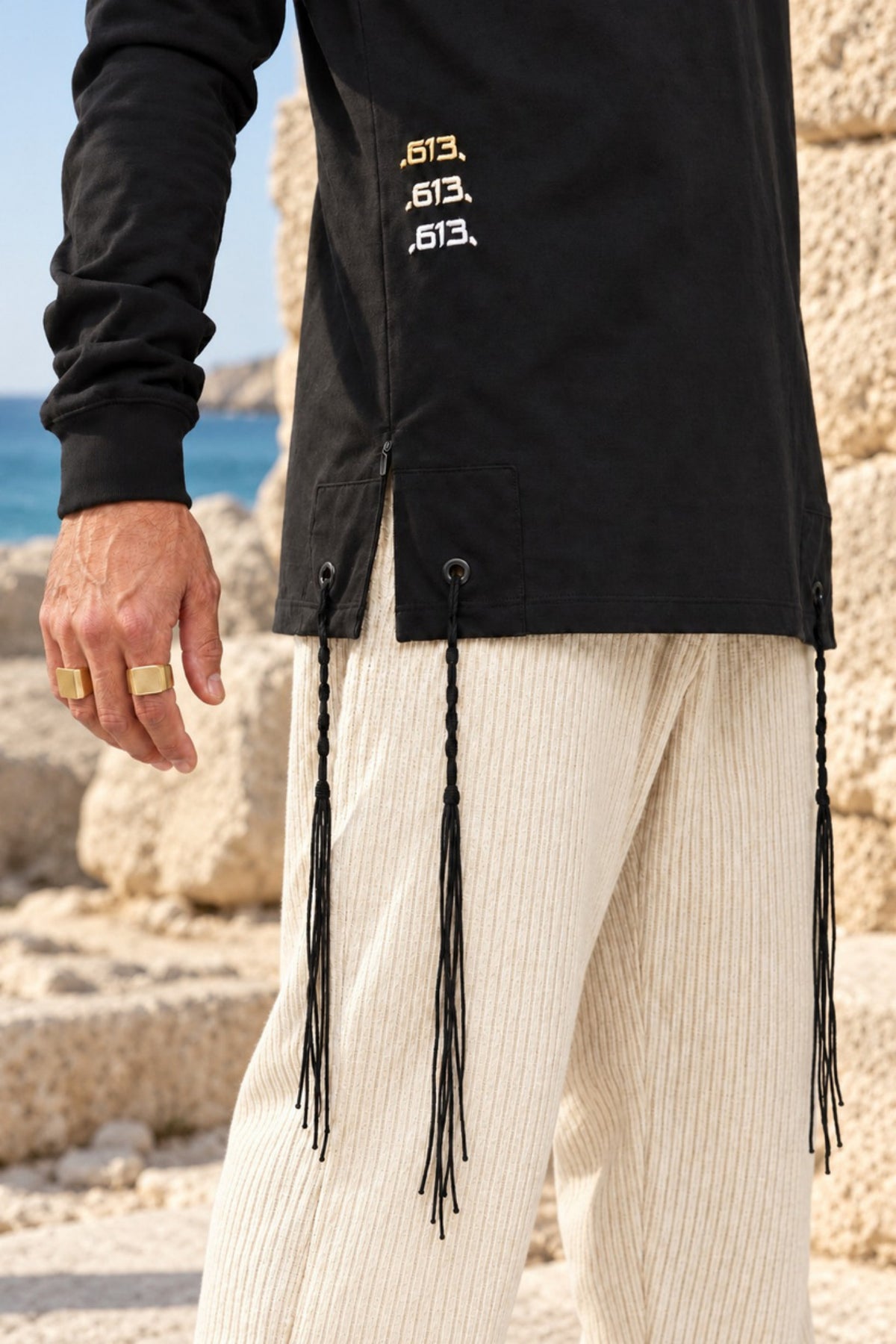 True Balance של 613, חולצת ציצית שחורה עם שרוול ארוך, צילום חוץ לצד מבני אבן